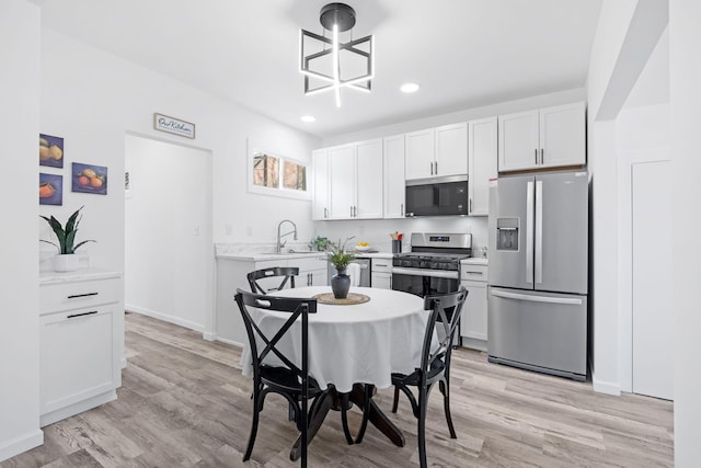 kitchen featuring light wood finished floors, stainless steel appliances, white cabinetry, a sink, and light stone countertops