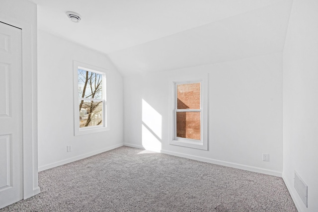 carpeted spare room with visible vents, vaulted ceiling, and baseboards