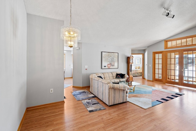 living room with light wood finished floors, vaulted ceiling, a textured ceiling, and french doors