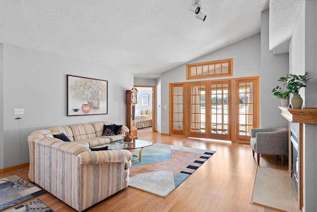 living room with french doors, lofted ceiling, light wood-style flooring, a textured ceiling, and baseboards