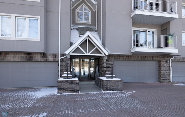 property entrance with a garage, brick siding, decorative driveway, and stucco siding