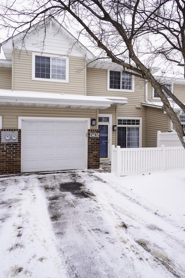 view of front facade featuring driveway, brick siding, and fence