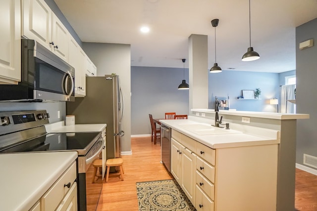 kitchen with appliances with stainless steel finishes, hanging light fixtures, light countertops, light wood-type flooring, and a sink