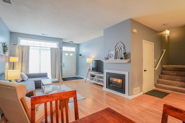 living area with visible vents, a glass covered fireplace, a textured ceiling, wood finished floors, and stairs