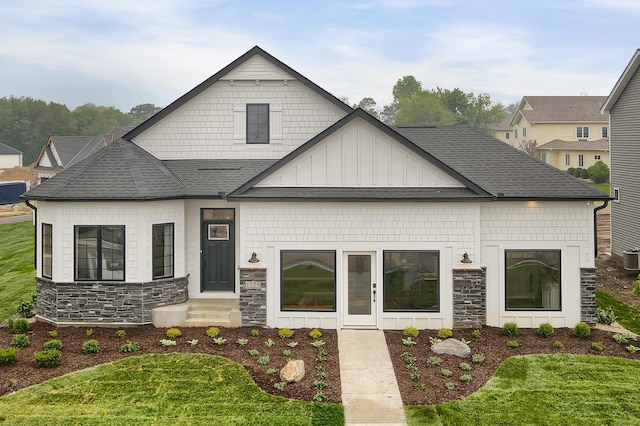 view of front facade with entry steps, stone siding, roof with shingles, a front lawn, and board and batten siding