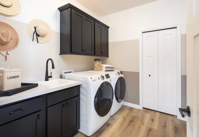 washroom featuring a sink, baseboards, light wood-style floors, cabinet space, and washing machine and clothes dryer