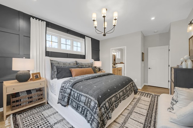 bedroom with baseboards, light wood-style flooring, ensuite bath, and an inviting chandelier