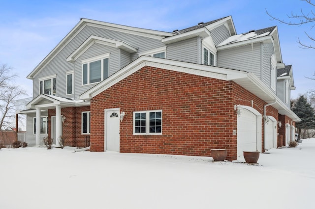 snow covered property featuring a garage and brick siding