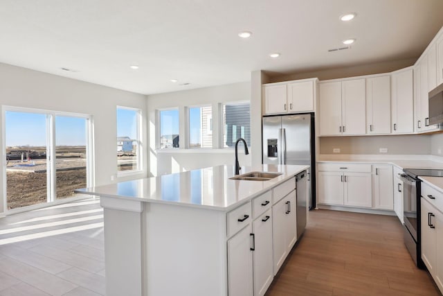 kitchen with a kitchen island with sink, stainless steel appliances, a sink, white cabinetry, and light countertops