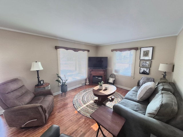 living room with crown molding, baseboards, wood finished floors, and a glass covered fireplace