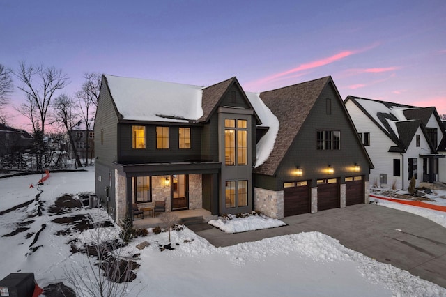 modern farmhouse featuring stone siding, a porch, an attached garage, and driveway