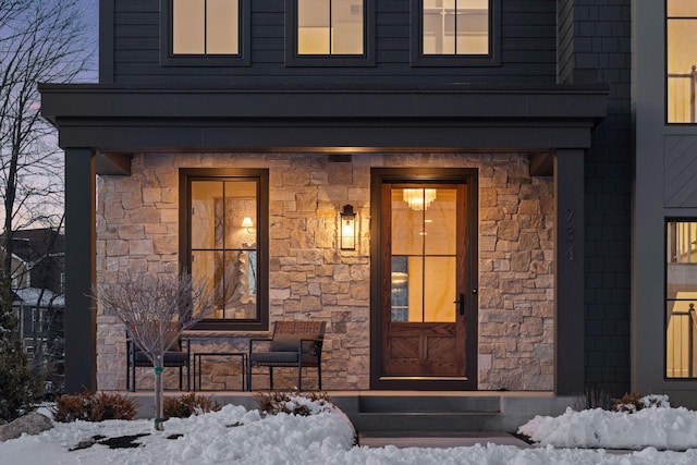 snow covered property entrance featuring covered porch and stone siding