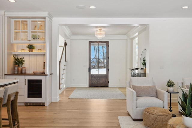 foyer featuring light wood finished floors, beverage cooler, ornamental molding, and a notable chandelier