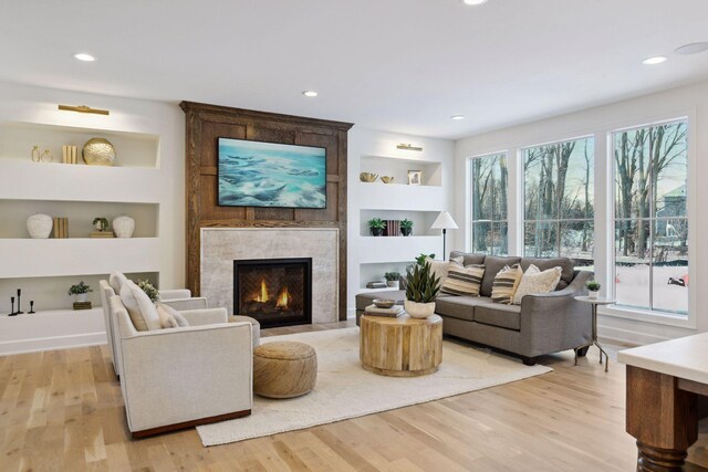 living room with light wood-type flooring, recessed lighting, built in features, and a tile fireplace