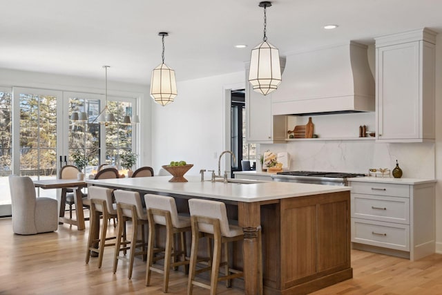 kitchen with light wood finished floors, decorative backsplash, light countertops, premium range hood, and a sink