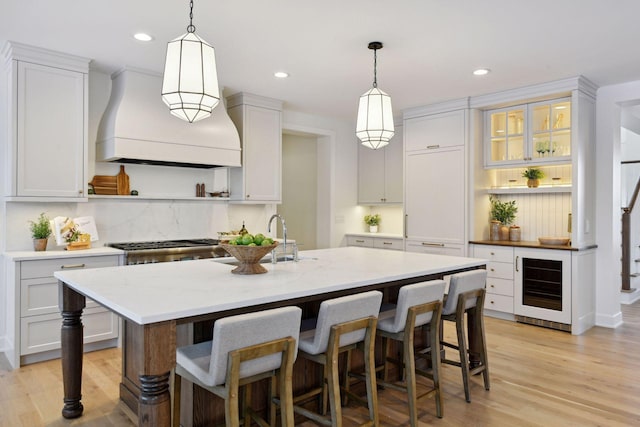 kitchen featuring beverage cooler, premium range hood, a kitchen breakfast bar, light wood-type flooring, and open shelves