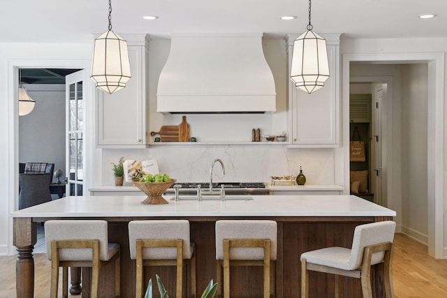 kitchen with custom range hood, decorative backsplash, a sink, and light countertops