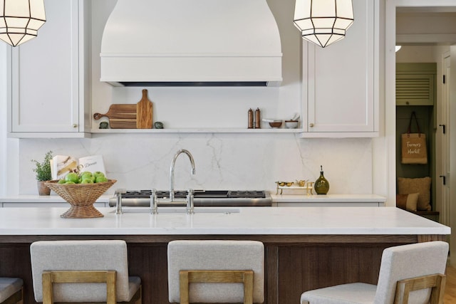 kitchen with open shelves, light countertops, decorative backsplash, a sink, and a kitchen breakfast bar