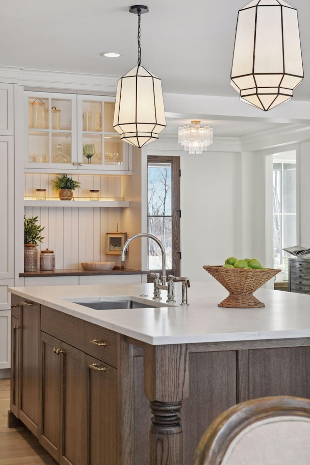 kitchen with glass insert cabinets, light countertops, a sink, and crown molding