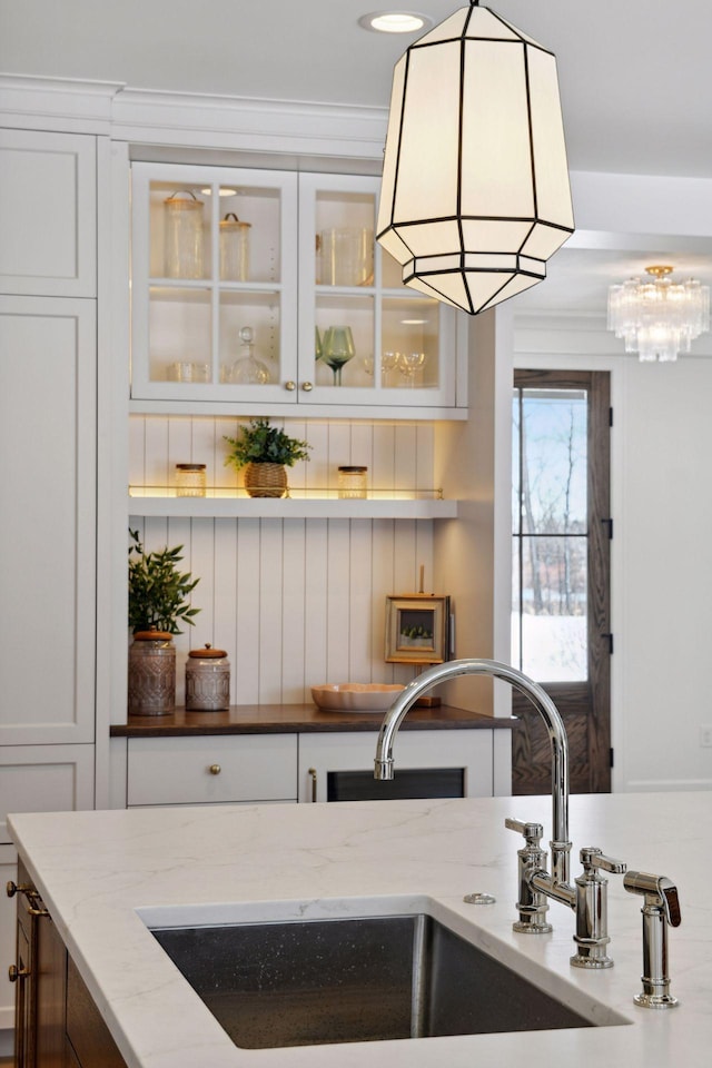 kitchen with light stone counters, a sink, glass insert cabinets, and white cabinets