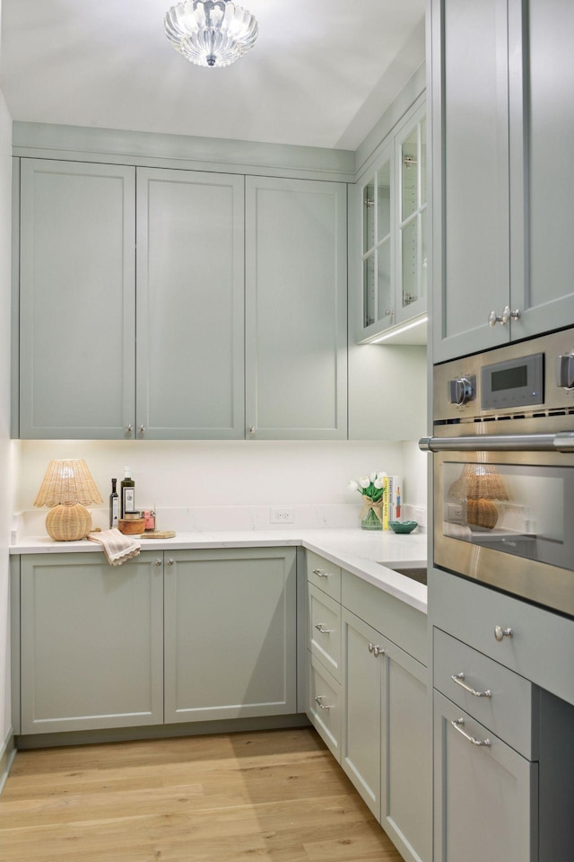 kitchen featuring glass insert cabinets, light wood-style floors, stainless steel oven, and light countertops