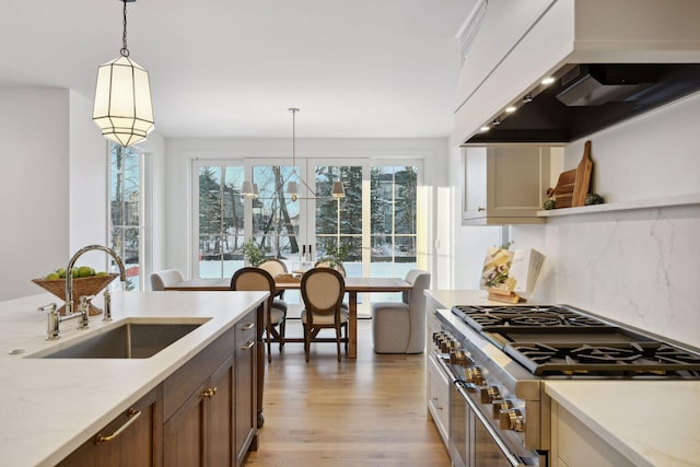 kitchen with pendant lighting, stainless steel stove, a sink, light wood-type flooring, and wall chimney exhaust hood