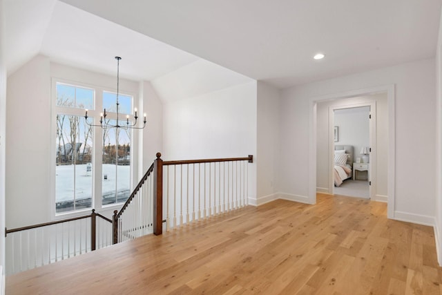 hallway with baseboards, lofted ceiling, an upstairs landing, light wood-type flooring, and a chandelier