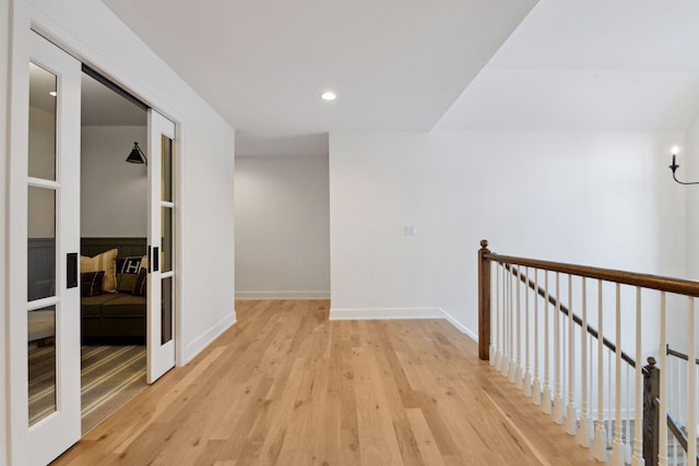 corridor with light wood-type flooring, baseboards, an upstairs landing, and recessed lighting