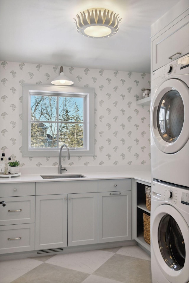 washroom with stacked washer and dryer, a sink, cabinet space, and wallpapered walls