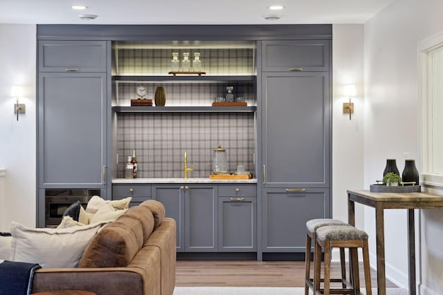 bar with indoor bar, light wood finished floors, recessed lighting, backsplash, and a sink