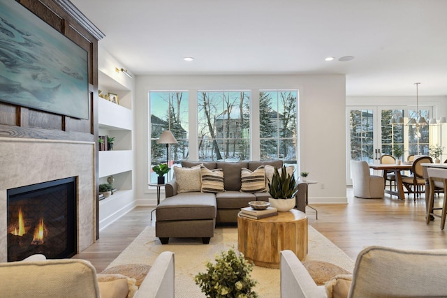 living area featuring built in shelves, recessed lighting, baseboards, light wood-type flooring, and a glass covered fireplace