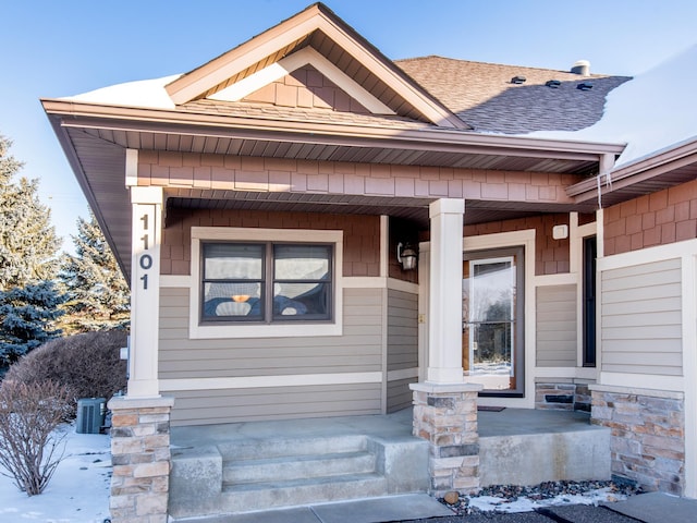 snow covered property entrance featuring covered porch and a shingled roof