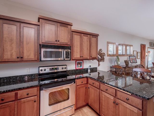 kitchen featuring appliances with stainless steel finishes, brown cabinetry, and dark stone countertops