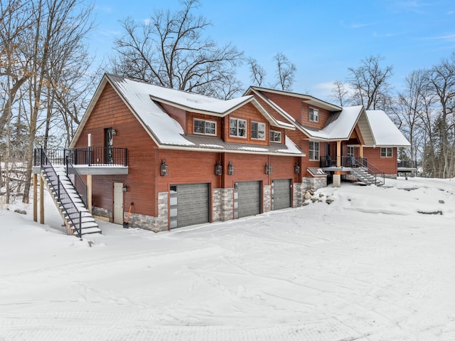 view of snow covered exterior with stone siding, stairway, and an attached garage