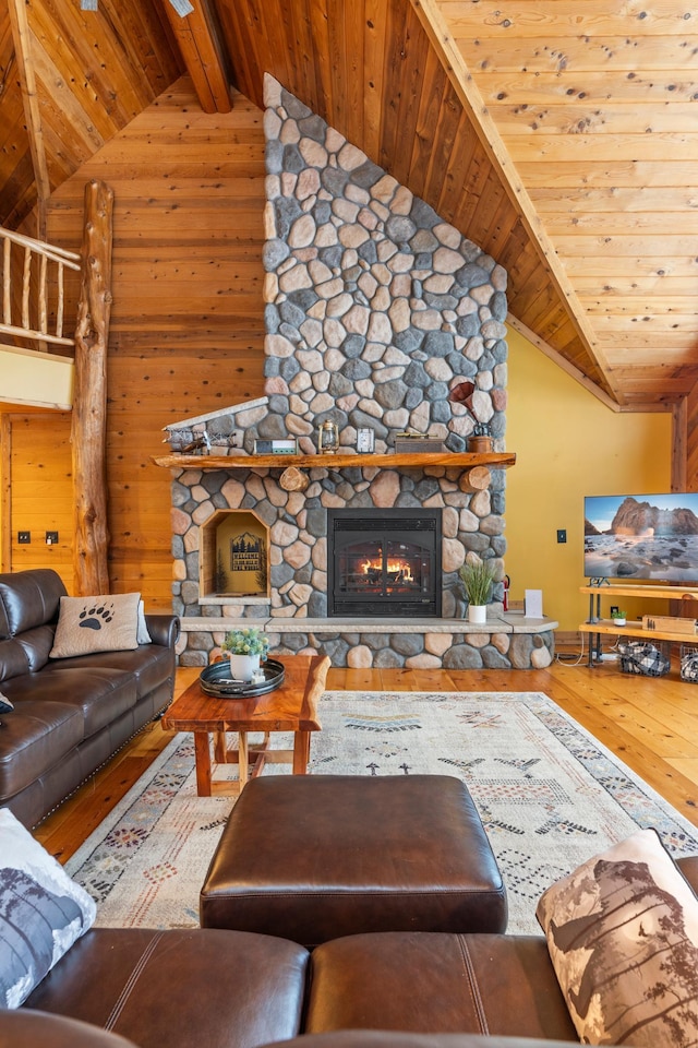 living area featuring hardwood / wood-style floors, wooden walls, a stone fireplace, vaulted ceiling with beams, and wood ceiling