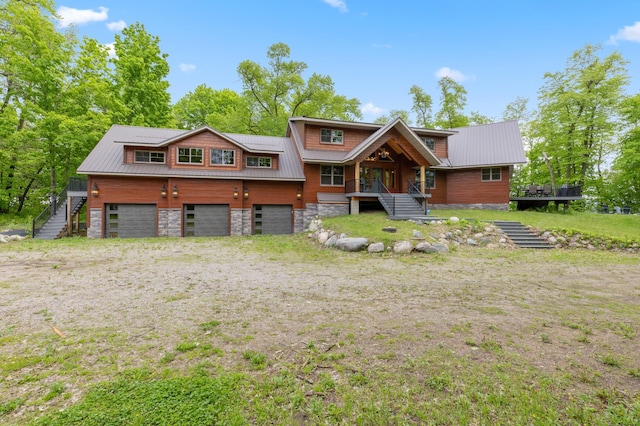 view of front facade featuring an attached garage, stairway, stone siding, and metal roof