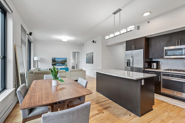 kitchen with dark brown cabinetry, a kitchen island, open floor plan, hanging light fixtures, and appliances with stainless steel finishes