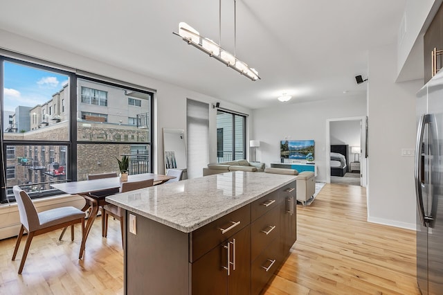 kitchen with dark brown cabinetry, a city view, stainless steel fridge with ice dispenser, a center island, and pendant lighting