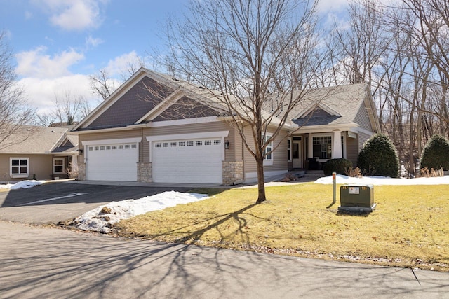 view of front of home featuring aphalt driveway, a garage, stone siding, and a front yard