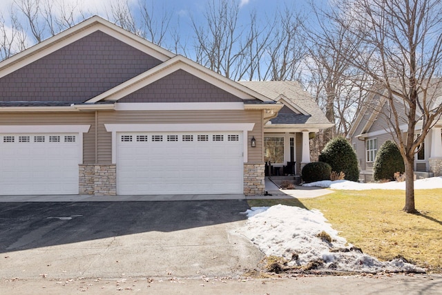 craftsman-style house featuring stone siding, driveway, an attached garage, and a front lawn