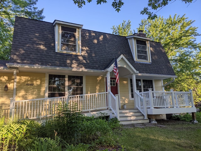 view of front facade with a porch, roof with shingles, and a chimney