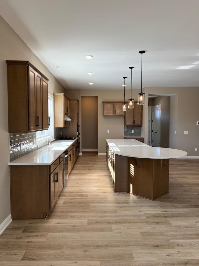 kitchen with light countertops, a kitchen island, decorative light fixtures, and brown cabinets