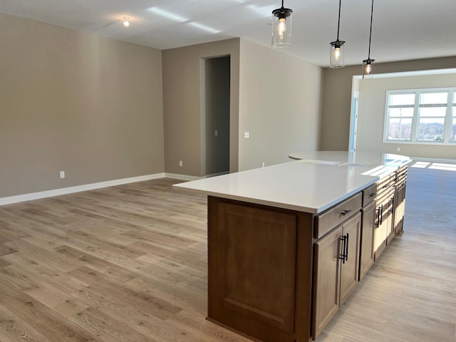 kitchen featuring open floor plan, a center island, hanging light fixtures, light countertops, and light wood-style floors