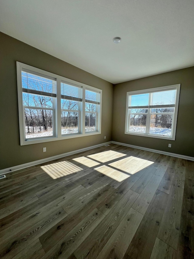 empty room with dark wood-style flooring, visible vents, and baseboards