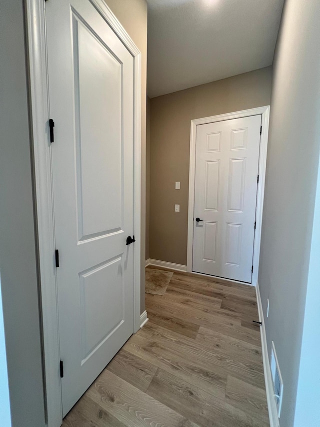 hall featuring baseboards, visible vents, and light wood finished floors