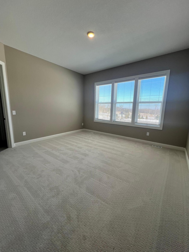 carpeted empty room featuring a textured ceiling and baseboards