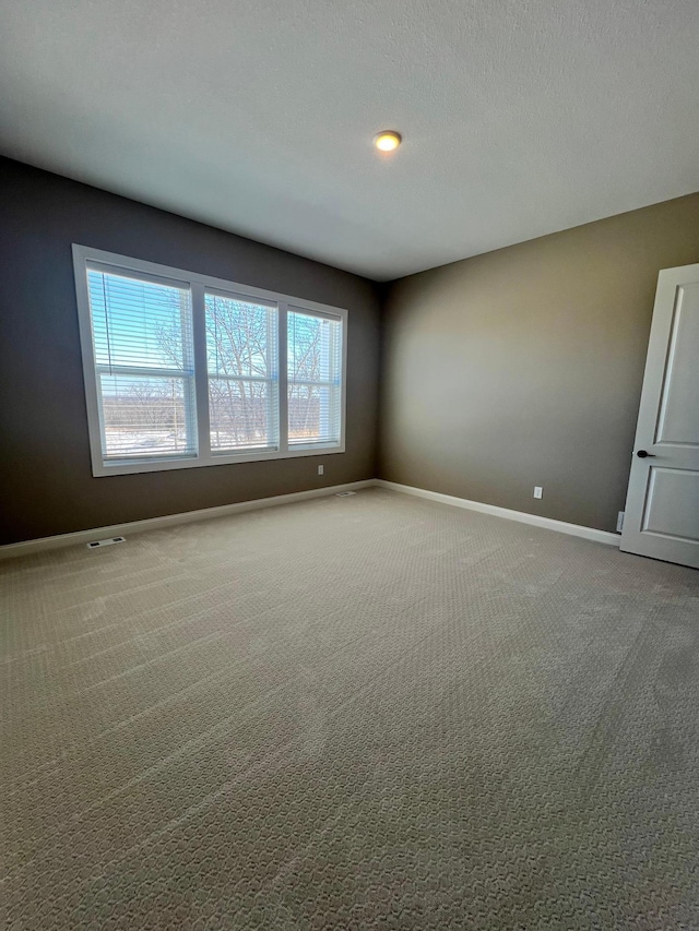 spare room with carpet floors, visible vents, a textured ceiling, and baseboards