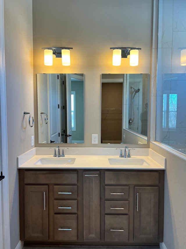 bathroom featuring double vanity, tiled shower, a sink, and a walk in closet