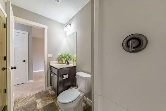 bathroom featuring toilet, stone finish floor, vanity, a textured ceiling, and baseboards