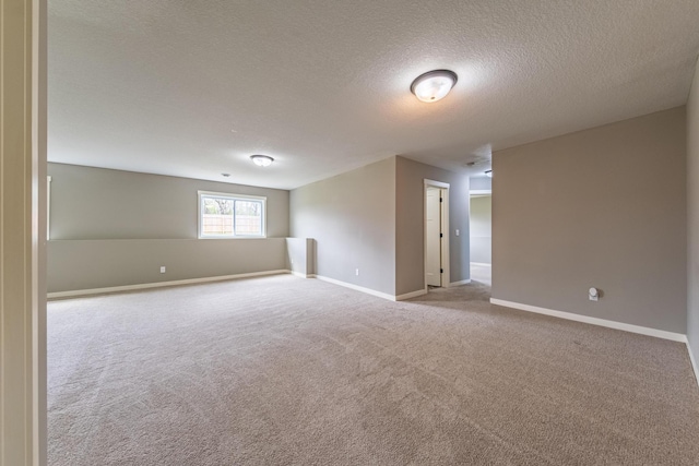 spare room featuring baseboards, a textured ceiling, and light colored carpet